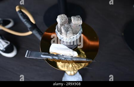 Sindelfingen, Germania. 29 giugno 2023. Pezzi di carbone per riscaldare il tabacco giacciono su un tubo dell'acqua di narghilè in un bar di narghilè. I shisha bar dominano sempre più il paesaggio urbano in molte città. Ma il mercato del narghilè soffre di troppe regole e burocrazia, criticano i giovani liberali nel Baden-Württemberg. (A dpa "i giovani liberali criticano la burocrazia per le barrette di narghilè”) credito: Bernd Weißbrod/dpa/Alamy Live News Foto Stock