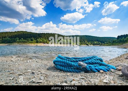 Corda blu su una spiaggia di ciottoli in estate con una grande foresta verde sullo sfondo Foto Stock