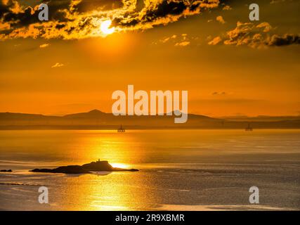 Tramonto arancione con il sole che tramonta tra le spettacolari nuvole sul Firth of Forth con vista sull'isola di Fidra e sulle Lomond Hills a Fife, Scozia, Regno Unito Foto Stock