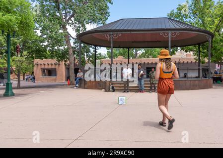 Una giovane donna che indossa un rustico colore arancio, short shot coordinati, cappello e top senza maniche cammina per mettere soldi nella scatola da collezione dei lavoratori di strada Foto Stock