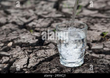 L'acqua viene versata in un bicchiere da bere posto su un terreno parcheggiato. Illustra la preziosità dell'acqua potabile in Europa. Wasserknappheit. Foto Stock