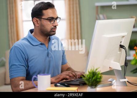 Rilassato libero professionista indiano che lavora al computer bevendo caffè a casa - concetto di rinfresco, dedizione e posto di lavoro Foto Stock