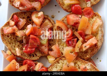 Friselle pugliese, tipica cucina estiva pugliese, Italia meridionale. Ciambelle croccanti a base di farina di grano duro condite con pomodori e olio d'oliva Foto Stock