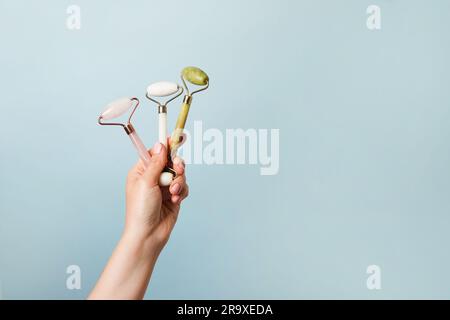 Rulli per massaggio facciale con giada e mani, gua Sha su sfondo blu. Cura della pelle, spazio copia Foto Stock