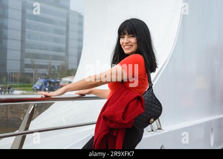 Giovane donna latina di etnia venezuelana vestita con contenuti rossi e neri sorridente guardando la telecamera in piedi sul Puente De la Mujer di Buenos Aires Foto Stock