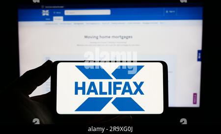 Persona che possiede uno smartphone con il logo della società britannica di servizi finanziari Halifax sullo schermo di fronte al sito Web. Concentrarsi sul display del telefono. Foto Stock