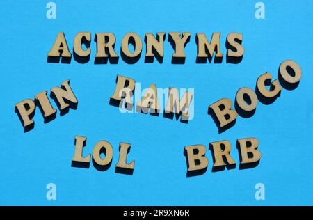 Acronimi, inclusi PIN, LOL, BRB, BOGO e RAM in lettere alfabetiche in legno isolate su sfondo blu Foto Stock