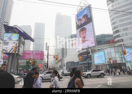 Toronto, Ontario/Canada - 28 giugno 2023: Con un indice di qualità dell'aria molto scarso di PM 2,5 (oltre 200) e 10, a causa di incendi boschivi nel nord e nell'ovest, i torontoniani e le auto stanno affrontando i rischi salutari e stanno attraversando il trafficato incrocio del centro di Yonge e Dundas. Alcune persone indossano maschere. Toronto era considerata una città tra le peggiori emissioni di aria inquinata quel giorno. Per uso editoriale Foto Stock