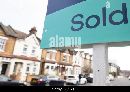 Agente immobiliare VENDUTO segno con defocused strada di case sullo sfondo Foto Stock