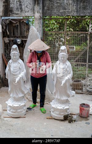 Saigon, Vietnam, 23 marzo 2023. Una donna vietnamita che sta lavorando su alcune statue consulta il suo telefono cellulare Foto Stock
