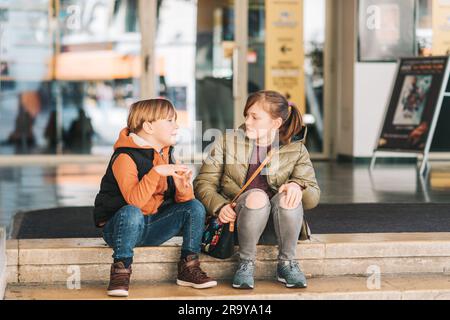 Gruppo di due bambini divertenti seduti sulle scale accanto al cinema, che hanno una discussione interessante Foto Stock