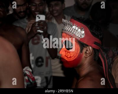 persone in pubblico che scattano foto di un artista theyam decorato con un viso luminoso dipinto e trucco durante un evento religioso tradizionale tenutosi in kerala, ind Foto Stock