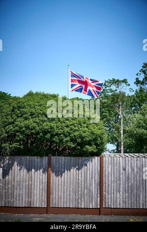 Union Jack su palo da bandiera che vola sopra la recinzione del giardino e gli alberi, St Annes, Regno Unito Foto Stock