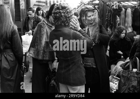 East End London anni '1970, donne che fanno shopping lungo il Roman Road Market, un elegante East Ender prova su una parrucca riccia alla moda, Tower Hamlets, Londra, Inghilterra 1975. 70 UK HOMER SYKES Foto Stock