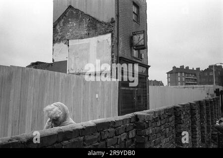 Povertà Londra anni 1970 Regno Unito, in un vicolo al largo di Whitechapel High Street, si inchinò contro il freddo, un anziano residente lotta contro l'orologiaio e gioielliere L. Elgrod, che si erge da solo sfidando il costruttore immobiliare e il team di demolizione. Whitechapel, Londra, Inghilterra 1975 UK HOMER SYKES Foto Stock