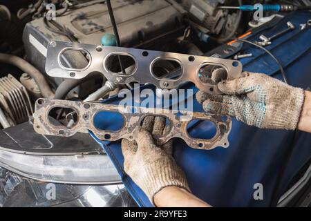 Meccanico automatico che tiene davanti a sé le guarnizioni del collettore vecchie e nuove per il motore di autovetture, servizio post-garanzia presso la stazione di ispezione tecnica Foto Stock