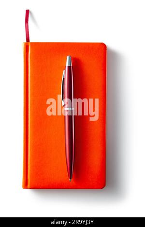 Blocco note chiuso di colore arancione e penna a sfera rossa isolata Foto Stock