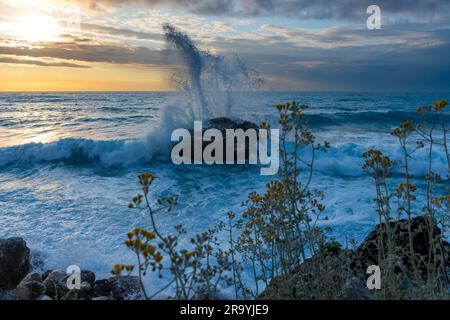 Un paesaggio marino di onde che si infrangono su una roccia durante il tramonto. Foto Stock