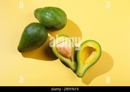 Vista dall'alto di un avocado tagliato a metà su una superficie gialla con avocado verde Foto Stock