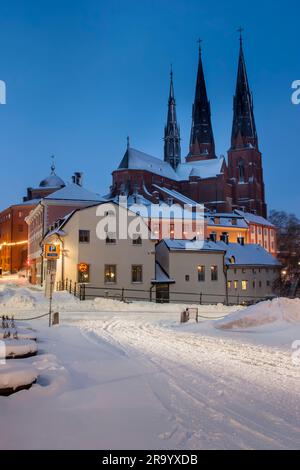 Strade innevate con case e cattedrale sullo sfondo con cielo azzurro. Uppsala, Svezia Foto Stock