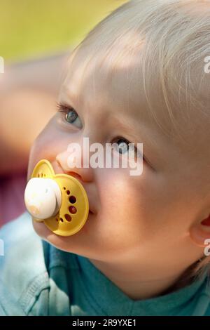 Primo piano del viso di un bambino che guarda in alto con il succhietto in bocca Foto Stock