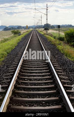 I binari ferroviari si trovano in un paesaggio sotto il cielo nuvoloso. Skane, Svezia. Foto Stock