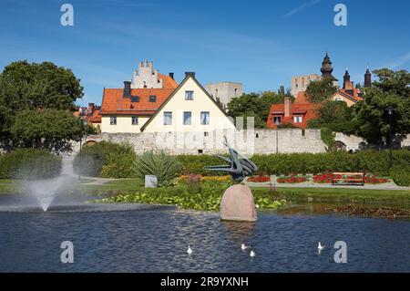 Fontana nello stagno del parco Almedalen con case sullo sfondo contro il cielo azzurro a Visby, Gotland, Svezia Foto Stock