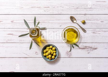 Natura morta con olive spagnole, olio extravergine di oliva spagnolo in bottiglie di vetro e contenitori e foglie di oliva e un cucchiaio di metallo su un tavolo di legno ma Foto Stock