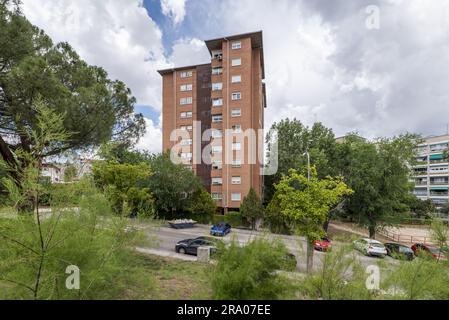 Vista di una torre residenziale solitaria urbana con una facciata in mattoni marrone circondata da una vegetazione lussureggiante Foto Stock