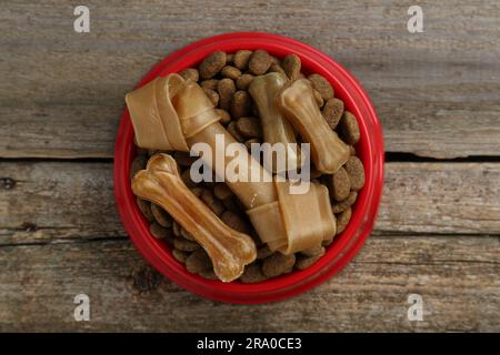 Cibo secco per cani e dolcetti (masticare le ossa) su pavimento in legno, vista dall'alto Foto Stock