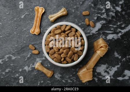 Cibo secco per cani e snack (masticando le ossa) su sfondo nero ruvido, piatto Foto Stock