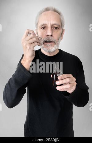 Un uomo maturo sta bevendo un cucchiaio di sciroppo per la tosse per curare il mal di gola e la bronchite Foto Stock