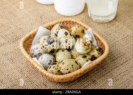 Uova di quaglia in un cestello di rattan, un bicchiere e una bottiglia di latte su una tovaglia di tela Foto Stock