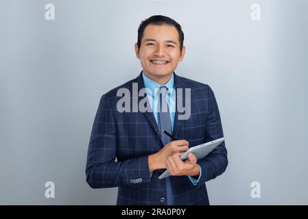 un giovane messicano dalla pelle scura sorride mentre punta il suo tablet aziendale, si veste di impiegato in ufficio in blu, una persona sola Foto Stock