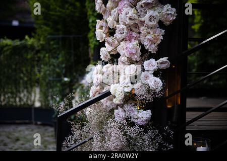 Bellissime composizioni di fiori arrossati per matrimoni con rose, candele e fiato del bambino in un lussureggiante evento con giardino botanico con scale e arco. Foto Stock