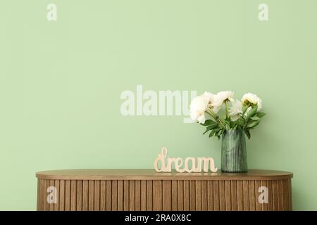 Vaso di peonie bianche e decorazioni a forma di SOGNO DI parole su comò vicino alle pareti verdi Foto Stock