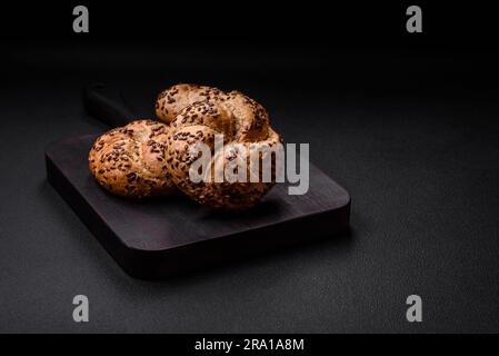Delizioso panino croccante appena sfornato o involtino kaiser con semi di sesamo su fondo di cemento scuro Foto Stock