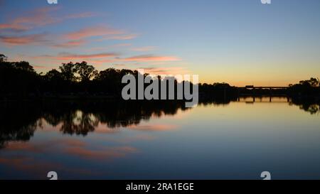 L'alba di una nuvola rosa riflessa nel fiume Murray a Mildura, con le gomme rosse del fiume lungo la riva del fiume dalla silhouette nera, è una natura scenografica Foto Stock