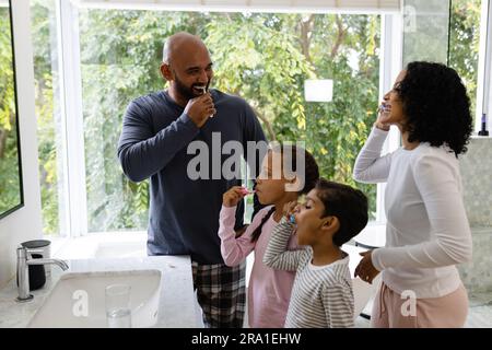 Felici e felici genitori birazziali, figlio e figlia che lavano i denti insieme in bagno la mattina Foto Stock