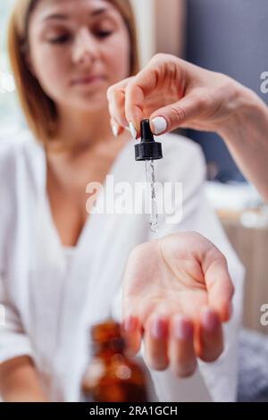 Primo piano della mano di un'estetista applicare il siero da una pipetta sul polso di una cliente femminile al chiuso. Selezione di olio essenziale in un salone o in una clinica. Con Foto Stock