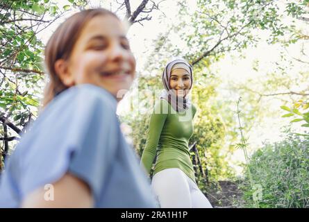 Due adolescenti felici di diverse nazionalità e fedi nel parco dopo l'allenamento. Ragazza caucasica in primo piano. Un adolescente musulmano in un hija Foto Stock