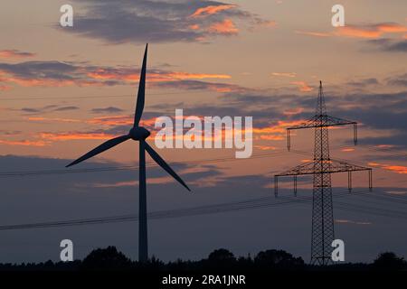 Centrale eolica e pilone di fronte al cielo serale, bagliore, tramonto, nuvole, Melbeck, Ilmenau, bassa Sassonia, Germania Foto Stock