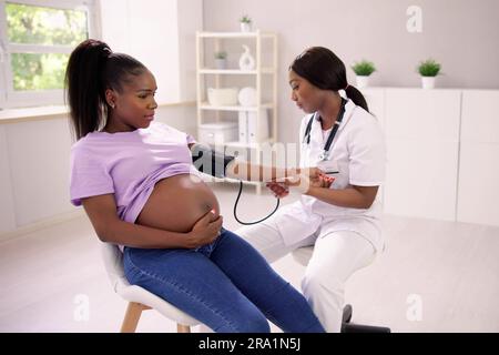 Primo piano del medico di Female misurazione della pressione sanguigna di donna incinta in clinica Foto Stock
