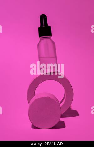 Siero facciale in flacone contagocce di vetro su podio bianco su sfondo rosa neon. Cosmetici naturali per la cura della pelle. Concetto di routine di bellezza. Composizione minima. Foto Stock