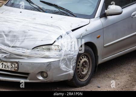 Novgorod Oblast, Russia - 27 aprile 2023: Vecchia auto in collisione con paraurti anteriore, faro e cofano danneggiati con nastro adesivo Foto Stock