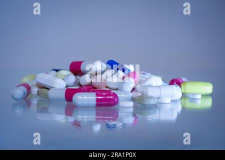 Pile di molte capsule e compresse di diversi colori e forme posizionate su un piano lucido, concetto di industria farmaceutica e controllo. Foto Stock