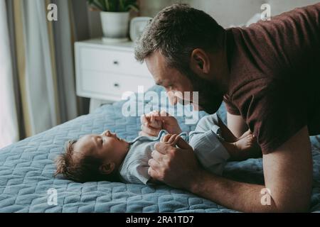 Papa' sta parlando con il bambino sul letto che gli tiene le mani Foto Stock