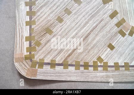 Impiallacciatura articolata con nastro in tela per il piano del tavolo da pranzo con motivo geometrico sul banco di lavoro nella vista ravvicinata superiore dell'officina Foto Stock