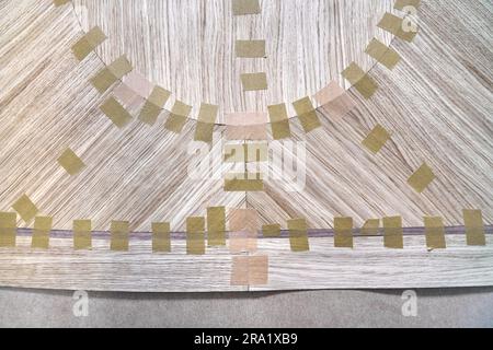 Impiallacciatura articolata con nastro in tela per il piano del tavolo da pranzo con motivo geometrico sul banco di lavoro nella vista ravvicinata superiore dell'officina Foto Stock