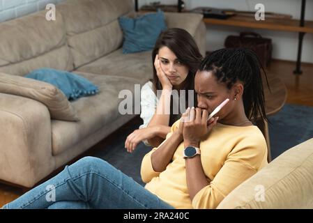 Giovane donna che cerca di confortare la migliore amica dopo aver ottenuto un test di gravidanza positivo a casa. Coinquilini a casa, una donna afroamericana è incinta di lei Foto Stock